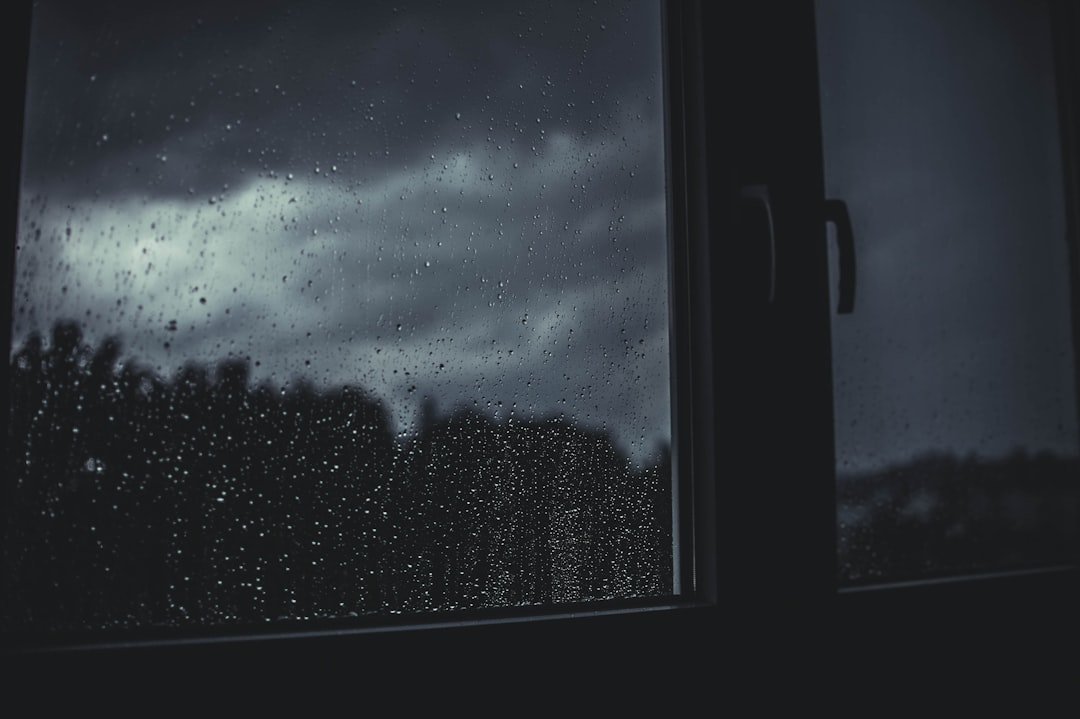 雨の夜、窓の向こうを見つめる人のシルエット
